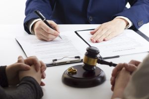 A lawyer in a suit discusses documents with clients. A gavel and wedding rings rest on the table, hinting at a legal process possibly related to divorce. This scene is common for Chicago divorce attorneys, who skillfully address complex issues like dad rights in divorce proceedings.